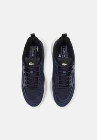 Lacoste tenevke v temno modri barvi z mrežastimi in gladkimi paneli, z belo podplatom, vezalkami in logotipom na ježku.