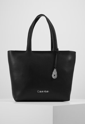 Sac cabas Calvin Klein en cuir noir texturé avec deux poignées et un petit pendentif cadenas argenté suspendu près du bord supérieur.