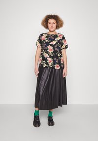 Black floral short-sleeve top with pink and blue flowers, paired with a pleated black maxi skirt, green socks, and black shoes.