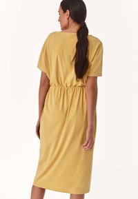 Senfgelbes Midi-Kleid mit kurzen Ärmeln, tailliertem Schnitt und seitlichen Taschen, aus weichem Stoff mit glatter Textur.