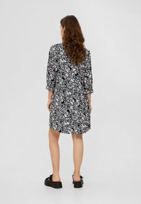 Schwarz-weiß gemustertes Kleid mit Dreiviertelärmeln, tailliertem Bund und einem fließenden Rock. Kombiniert mit klobigen schwarzen Plateauschuhen.
