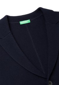 Donkerblauwe gebreide cardigan met een sjaalkraag, knoopsluiting en een gestructureerde stof. Voorzien van een groen label bij de hals.