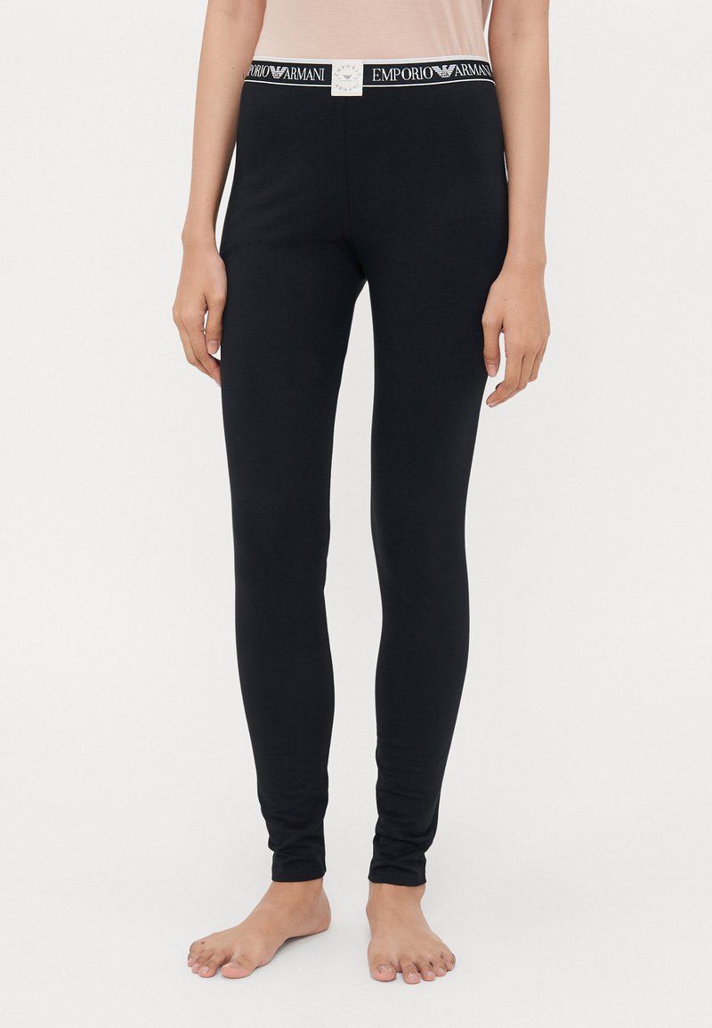 Svarta leggings tillverkade av mjukt tyg med en åtsittande passform. Har en vit midja med "Emporio Armani"-logotypen tydligt synlig.