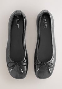 Paire de ballerines noires à motif crocodile avec petits nœuds et semelles plates, vues de dessus sur un fond clair.