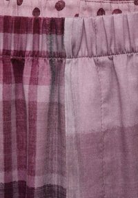Tissu violet avec un mélange de teintes plus claires et plus foncées, présentant un motif à carreaux et des points ronds. Texture douce avec une taille élastique.