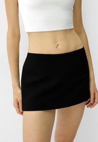 Svart mini kjol med en slät textur, med en enkel design och rak fåll, i kombination med en figurnära vit crop top.