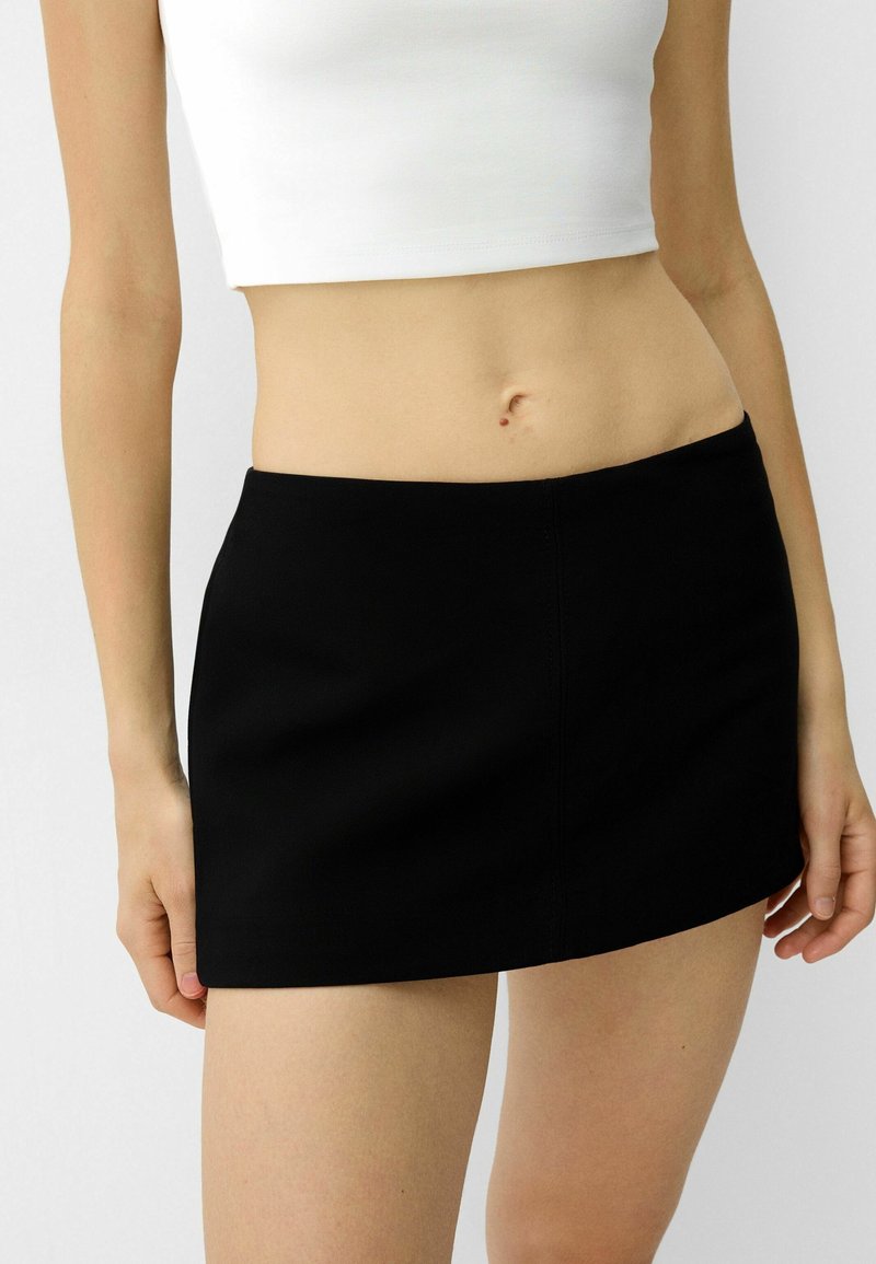 Svart mini kjol med en slät textur, med en enkel design och rak fåll, i kombination med en figurnära vit crop top.