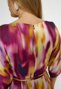Mehrfarbiges Kleid aus einem glatten, fließenden Stoff mit einem lebhaften abstrakten Muster in Pink, Gelb und Lila sowie einem Reißverschluss im Rücken.