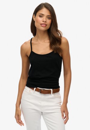 Top aderente nero con spalline sottili, abbinato a pantaloni bianchi e una cintura marrone. Tessuto liscio con un design semplice e senza motivi.