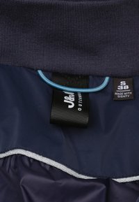 Navyblauwe jas met een geribde kraag, elastische trekkoord, zilverrandvoering en labels die merk en maat aangeven.