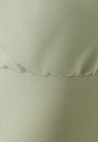 Peça de vestuário verde claro com uma textura suave e macia. Apresenta uma parte superior franzida e uma parte inferior justa, com um brilho subtil.