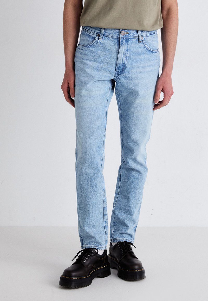 Vaqueros rectos de color azul claro hechos de denim, con cinco bolsillos y cremallera. Combinados con zapatos de plataforma negros para un contraste.