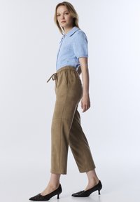 Haut tricot à manches courtes bleu clair avec col, associé à un pantalon tapered beige avec taille élastique et cordon de serrage. Talons aiguilles noirs.