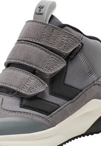 Szare buty sportowe wykonane z zamszu i materiałów tekstylnych, z rzepami, teksturowanym czarnym akcentem oraz kontrastującą białą podeszwą.