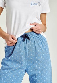 Biała bawełniana koszulka z napisem "Relax" w połączeniu z niebieskimi spodenkami do piżamy z granatowym sznurkiem i białym wzorem kotwicy na całej powierzchni.