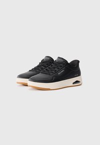 Black sneakers with a smooth leather upper, perforated detailing, and a contrasting white midsole. Features lace closure and visible air cushioning.