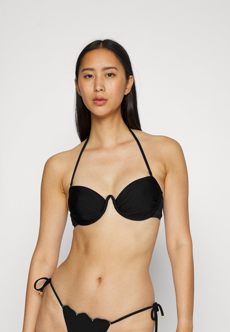 Conjunto de biquíni preto com um top bandeau com copas suaves e amarrações de pescoço, combinado com um fundo de corte baixo com bordas em forma de concha e fecho de laço.