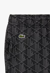 Zwart stof met een geometrisch patroon. Voorzien van een elastische tailleband en een klein groen geborduurd krokodillenlogo aan de zijkant.