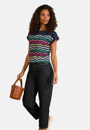 Haut à manches courtes bleu marine avec des motifs ondulés multicolores, associé à un pantalon en denim foncé et un sac seau marron. Ajustement et style décontractés.