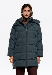 Długa, pikowana kurtka w ciemnozielonym kolorze, z zamkiem błyskawicznym, bocznymi kieszeniami oraz odpinanym kapturem o gładkim, błyszczącym wykończeniu.