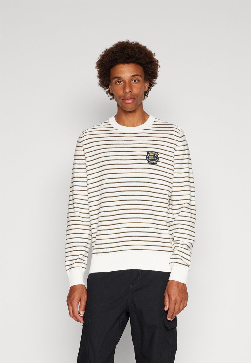 Gestreepte trui in crème en bruin, gebreide stof, ronde hals, geribde manchetten en zoom, met een rond logopatch op de borst.