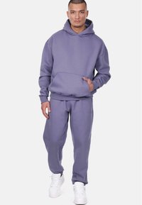 Purple hoodie and matching joggers in cotton blend. Features a front pocket, ribbed cuffs, and a relaxed fit. White sneakers complete the outfit.