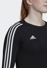 Schwarzes, athletisches Langarmoberteil mit weißem Dreistreifen-Design auf den Schultern und kleinem weißen adidas-Logo auf der Brust. Glatte Textur.