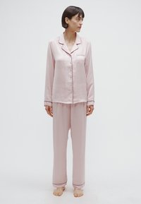 Ensemble de pyjama en satin rose avec manches longues et boutons, comprenant une poche poitrine, un passepoil contrastant et un pantalon ample.