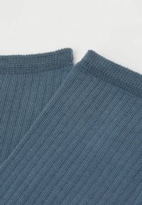 Calcetines azules de punto con una textura acanalada, que presentan un borde sin costura y un acabado suave, parcialmente superpuestos en la imagen.