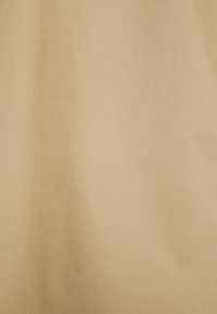 Texture de tissu marron clair avec une ombre verticale subtile et de légères rides, réparties uniformément sur toute la surface.