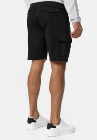 Shorts cargo noirs en coton, avec plusieurs poches latérales et des poches arrière plates. Associés à des baskets blanches avec des accents noirs.
