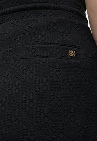 Μαύρη υφασμάτινη φούστα με ανάγλυφα σχέδια "HUGO" και ένα μικρό χρυσό καρφί με το λογότυπο "HUGO" κοντά στη μέση στο πίσω μέρος.