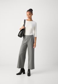 Vit, figurnära långärmad topp, hög midja grå vida byxor och svarta ankelskor. Svart handv�äska med en böjd design och silverdetaljer.