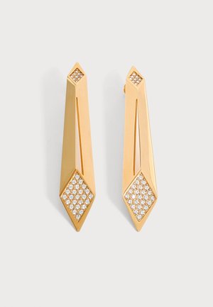 Boucles d'oreilles goutte géométriques en or avec extrémités en forme de diamant incrustées de petits cristaux clairs sur un fond clair uni.