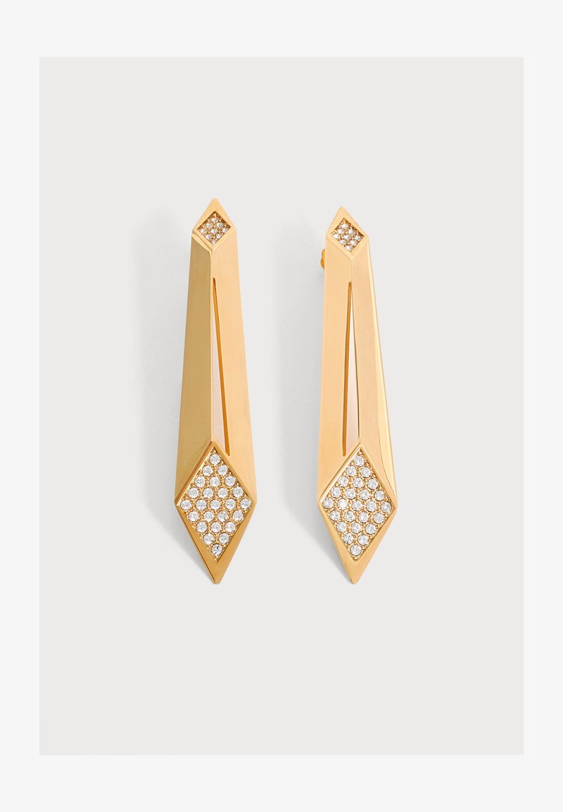 Boucles d'oreilles goutte géométriques en or avec extrémités en forme de diamant incrustées de petits cristaux clairs sur un fond clair uni.