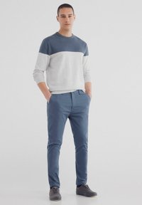 Tröja i ljusgrått och marinblått med ett horisontellt färgblockdesign; slim-fit blå byxor; grå skor med snören. Slät textur, avslappnad look.