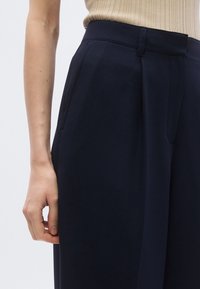 Navy trousers with a tailored fit, featuring soft fabric, a flat front, and side pockets. Seam detailing adds texture and structure.