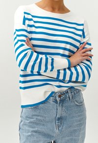 Gestreifter Pullover in Weiß und Blau mit rundem Ausschnitt und gerippten Bündchen, kombiniert mit hoch taillierten hellblauen Jeans. Weiche Stricktextur.
