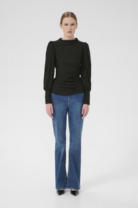 Black long-sleeve top with gathered details on one side, paired with blue flared jeans and black pointed-toe heels. Smooth fabric texture.