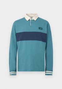 Μακρυμάνικο ράγκμπι μπλουζάκι σε τιρκουάζ με οριζόντια ναυτική ρίγα, λευκό γιακά, πατιλέτα με κουμπιά και ριγωτά μανσέτες.