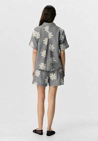 Ensemble deux pièces composé d'une chemise à manches courtes et col, ainsi que d'un short. Motif à carreaux gris avec de grandes fleurs blanches.