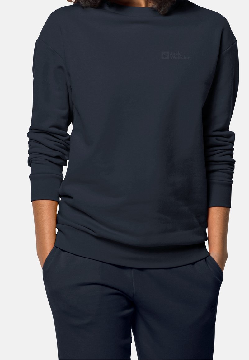 Löysä istuva tummansininen collegepaita pehmeästä kankaasta, leveällä kaula-aukolla ja käärityillä hihoilla. Rintakehässä hienovarainen logotyyppitys, yhdistettynä samaan sävyyn oleviin housuihin.