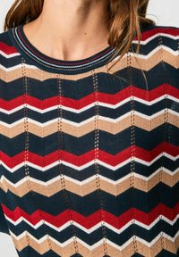 Pletený svetr se vzorem ve tvaru rybí kosti v námořnické modři, červené, bílé a béžové barvě. Má kulatý výstřih a krajkované detaily.