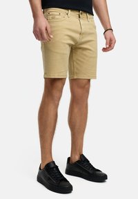 Shorts en kaki avec une coupe droite, un design à cinq poches et une légère décoloration ; associés à des baskets noires avec une texture lisse et un système de laçage.