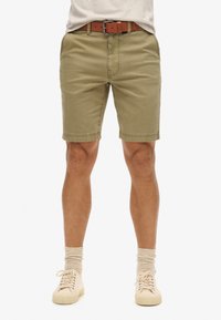Olijfgroene shorts van katoen, met voorzakken, een rechte pasvorm en een zoom boven de knie, gecombineerd met een bruine riem en beige schoenen.
