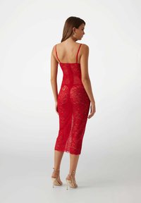 Red lace dress with a fitted design, mid-calf length, spaghetti straps, and a back zipper. Features a floral lace pattern and sheer texture.