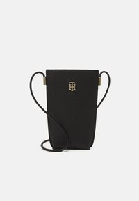 Czarna, teksturowana skórzana torebka typu crossbody z wąskim paskiem i złotym logo umieszczonym na środku z przodu.