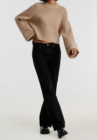 Suéter corto de punto beige con puños anchos acanalados, combinado con vaqueros negros acampanados y botines negros. Textura lisa, ajuste relajado.