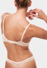 Lace beha en string set in nude, met verstelbare bandjes, bloemenpatronen en een haak-en-oogsluiting op de rug. Zachte textuur.