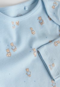 Ljusblå bomullspyjamas med ett mönster av små nallar i randiga kläder, med rund halsringning och korta ärmar.